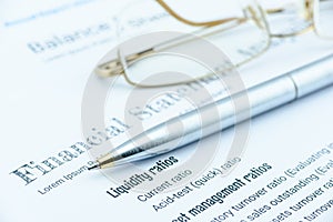 Blue ballpoint pen and eye glasses on a company's financial analysis check list.