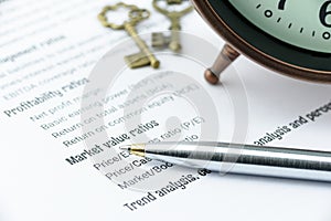 Blue ballpoint pen on a financial ratios analysis check lists with an antique clock and two vintage brass keys.