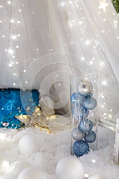 Blue baubles in glass vase. Christmas tree toys and New Year decorations. Unfocused white background with shiny sparkling garland