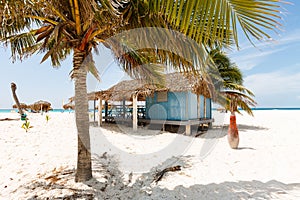 Blue beach house with small veranda, thatched roof standing on beach near ocean