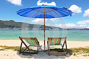 A blue beach umbrella and striped chaise lounges