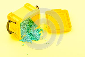 Blue beads are poured out of a yellow plastic container onto a yellow surface