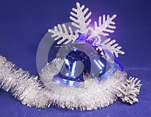 Blue beautiful New Year`s ornament - a hand bell with a bow, brilliant tinsel, silver cones and a snowflake on a blue background