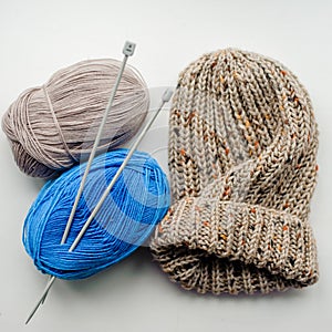 Blue and beige knitted wool skeins and a knitted hat on a light background. Alpaca, merino yarn. Threads for knitting and