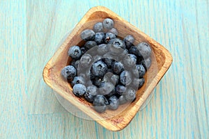 Blue berries in wooden bowl on a green wooden background