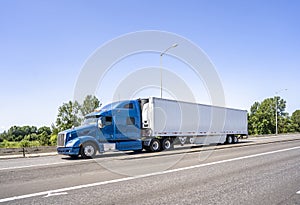 Blue big rig classic semi truck with high cab transporting load in refrigerator semi trailer running on the highway road entrance