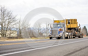Blue big rig heavy duty semi truck with oversize load equipment on the step down semi truck moving on the public road