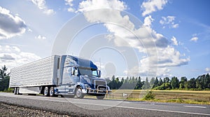 Blue big rig semi truck with grille guard trabsporting frozen cargo in refrigerator semi trailer with skirt spoiler running on the