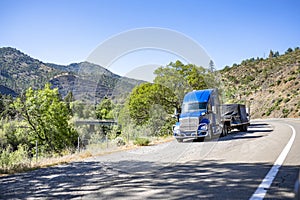Blue big rig semi truck with loaded step down semi trailer take a break standing on the mountain road shoulder by the river