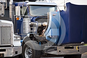 Blue big rig semi truck with open hood standing on the parking lot for repair engine and service work