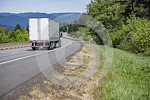 Blue big rig semi truck tractor transporting cargo in dry van semi trailer running for delivery on the winding highway road in a