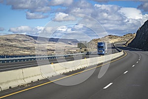 Blue big rig semi truck transporting cargo in dry van semi trailer driving on the winding mountain highway road along the river