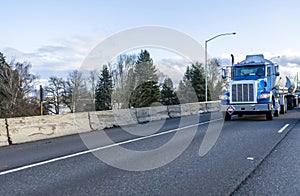 Blue big rig semi truck transporting fuel cargo in two tank semi trailer driving on the wide straight highway