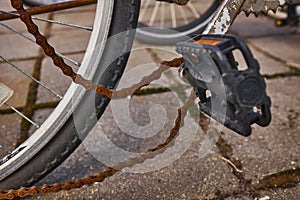 Blue bike has been outside all winter and got broken. Rusty bicycle chain hangs on sprocket and gear.