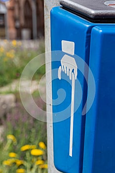 Blue bin outdoors in a street with hand with cane