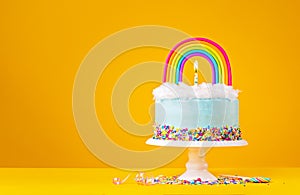 Blue Birthday Cake with Rainbow topper on Yellow Background
