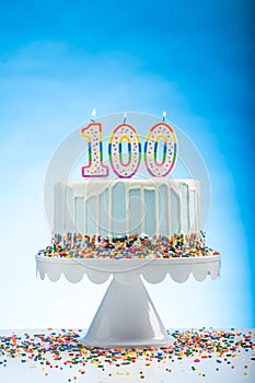 Blue Birthday Cake with Sprinkles on a White Cake Plate and Blue Background with 100 candles on Top