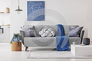 Blue blanket and grey knot pillow on trendy sofa in chic living room