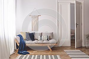 Blue blanket and pillows on wooden couch in white living room interior with rugs and door. Real photo