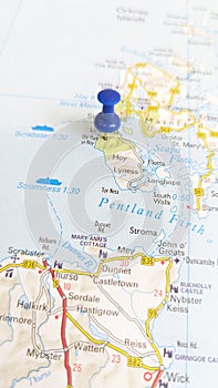 A blue board pin stuck in the island of Hoy on a map of Scotland portrait