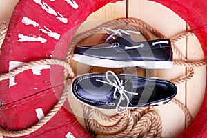 Blue boat shoes on wooden background near red lifebuoy and rope