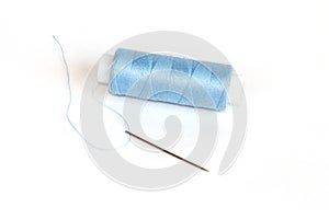 Blue bobbin of thread with needle on white
