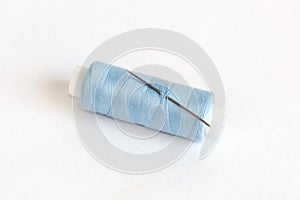 Blue bobbin of thread with needle on white