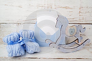 Blue booties for the baby, envelop with empty card on a wooden background and wooden horse.