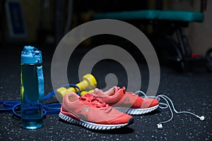 A blue bottle, crimson sneakers, a mobile phone with headphones, two yellow dumbbells on a dark blurred background.