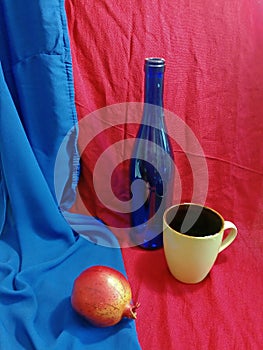 Blue bottle on red and pomegranate on blue drapery