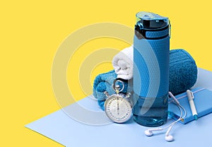 Blue bottle of water, towels, headphones, stopwatch and notepad. Sports equipment on creative background