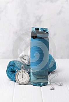 Blue bottle of water, towels, headphones and stopwatch. Sports equipment on white wooden background