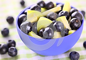 Blue bowl full of blueberries and pieces of apple with blueberries around it