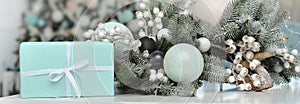 Blue box with a gift near a beautiful Christmas composition of snow-covered Christmas tree branches, New Year`s balls, snow-