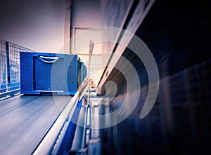 Blue boxes in a large, fully automated logistics warehouse run on a conveyor belt. Background is blurred