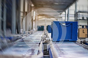 Blue boxes in a large, fully automated logistics warehouse run on a conveyor belt. Background is blurred. It is a modern storage