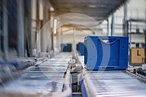 Blue boxes in a large, fully automated logistics warehouse run on a conveyor belt. Background is blurred. It is a modern storage
