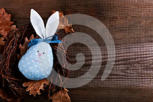 Blue Bunny Easter egg handmade with pretty face lying in a nest on a wooden background. Copy space