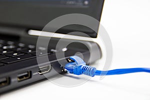 Blue cable network connection to a Lan port of laptop computer on white table