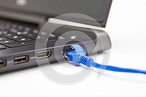 Blue cable network connection to a Lan port of laptop computer on white table