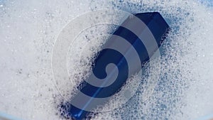 A blue can of shampoo floats in foamy water. The concept of cleanliness and personal care.