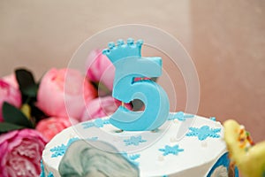 Blue candle with number 5 and crown on top of winter birthday cake with snowflakes. Frozen cartoon character