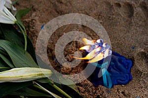 Blue candles with a lit flame and a white flower on the beach sand. Gift for Iemanja the queen of the sea