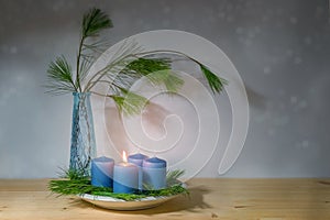 Blue candles, one is lit for the first advent, and a vase with pine branches, modern decoration in the Christmas season