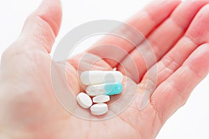 Blue capsule medicines and tablets in female hand.