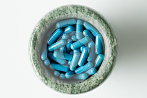 Blue capsules and orange pills with mortar pestles on white background.