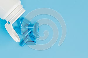 Blue capsules, pills on a blue background. Capsules in a white jar. Vitamins, nutritional supplements for women`s health