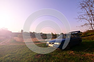 A blue car on a background of a rustic landscape with a wild cane field and a small lake. The family came to rest on the nature n