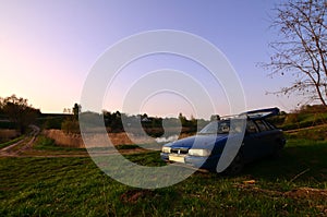 A blue car on a background of a rustic landscape with a wild cane field and a small lake. The family came to rest on the nature n