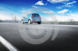 A blue car driving fast on the countryside road against sky with